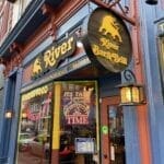 the Entrance of River Bar  Grill One of the Best Bars in Frederick Features a Round Wooden Sign with a Golden Bull and Yellow Lettering the Blue and Orange Exterior Boasts Mexican Food and Its Taco Time Signs Decorative Lanterns and Brick Details