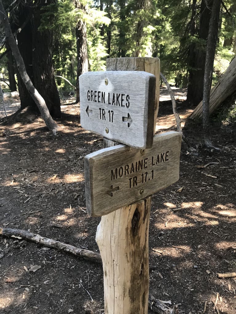 Two weathered wooden trail signs stand in a sun-dappled forest, guiding hikers on Green Lakes TR 17 and Moraine Lake TR 17. Surrounded by pines, this spot marks one of the classic Bend hikes for those exploring trails near Bend, Oregon.
