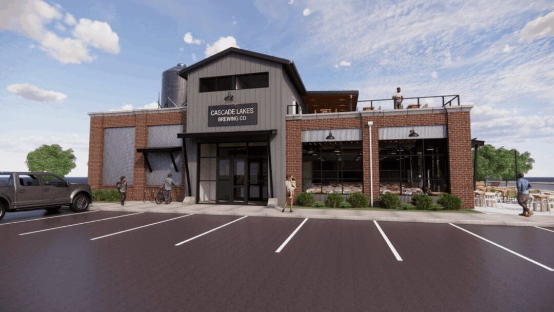 a Modern Brick and Metal Building with Large Windows and a Sign Reading Cascade Lakes Brewing Co is Showna Lively Spot Among Breweries in Bend Oregon People Gather by the Entrance and on the Patio Enjoying Outdoor Seating on a Sunny Day