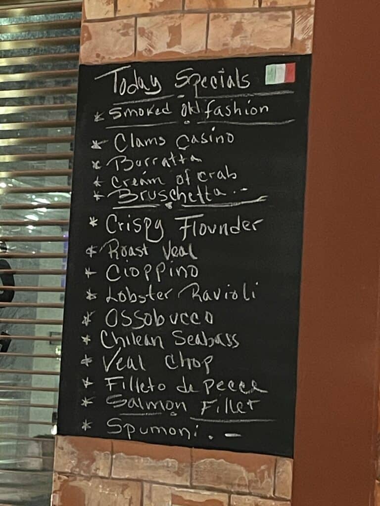 a Black Chalkboard Menu on a Brick Wall Lists Todays Specials in White Handwritten Text Showcasing Favorites Found at Frederick Italian Restaurants Like Cioppino Lobster Ravioli Osso Buco Burrata and Spumoni