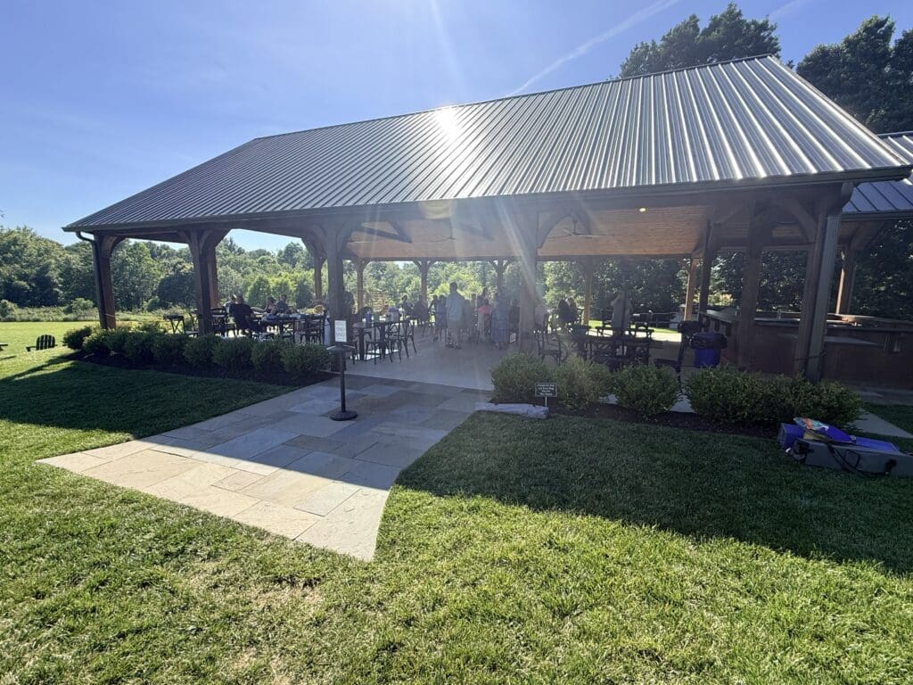 Outdoor Pavilion with a Tall Metal Roof Wood Columns and People Dining at Tables in Bright Sun