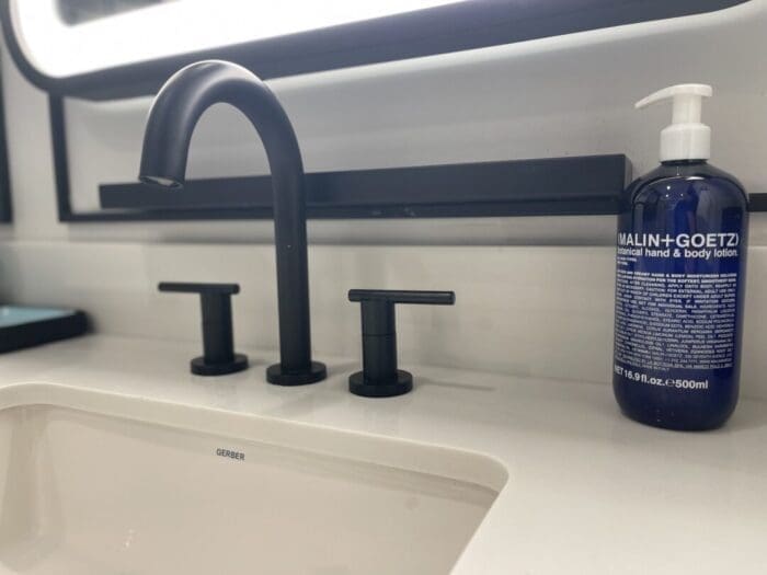 Modern Bathroom Sink with a Matte Black Faucet and Handles at Visitation Hotel Frederick Md to the Right a Blue Malin+goetz Hand and Body Lotion Bottle with a White Pump Rests on a White Countertop Under a Rectangular Mirror
