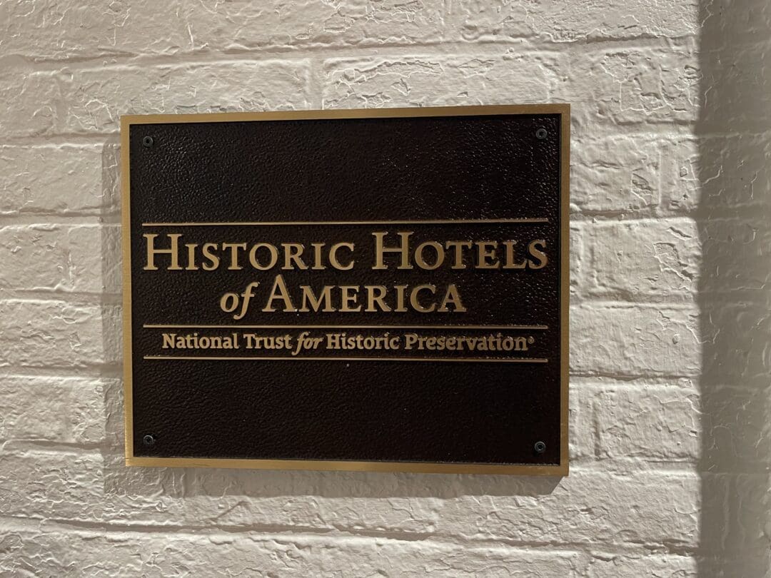 A dark plaque on a white brick wall reads: Historic Hotels of America. National Trust for Historic Preservation® in gold lettering, honoring Visitation Hotel Frederick MD as a recognized historic hotel.