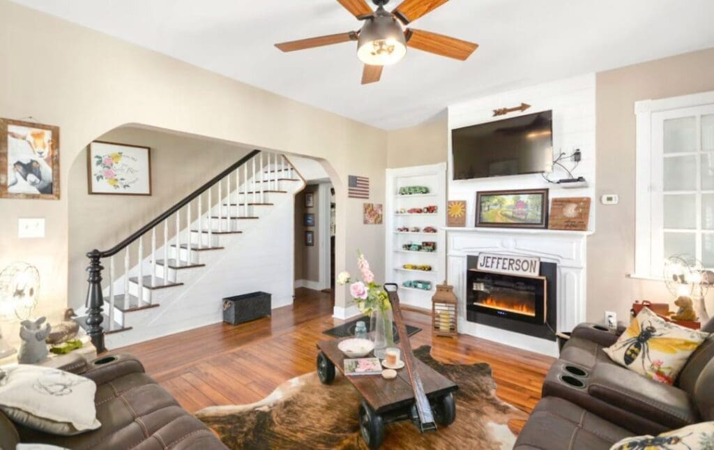 Cozy Living Room in This Airbnb Frederick Md Features Hardwood Floors Two Brown Recliners a Cowhide Rug Coffee Table Fireplace with jefferson Sign Wall mounted Tv Shelves with Toy Cars Stairs with White Risers and Black Railing