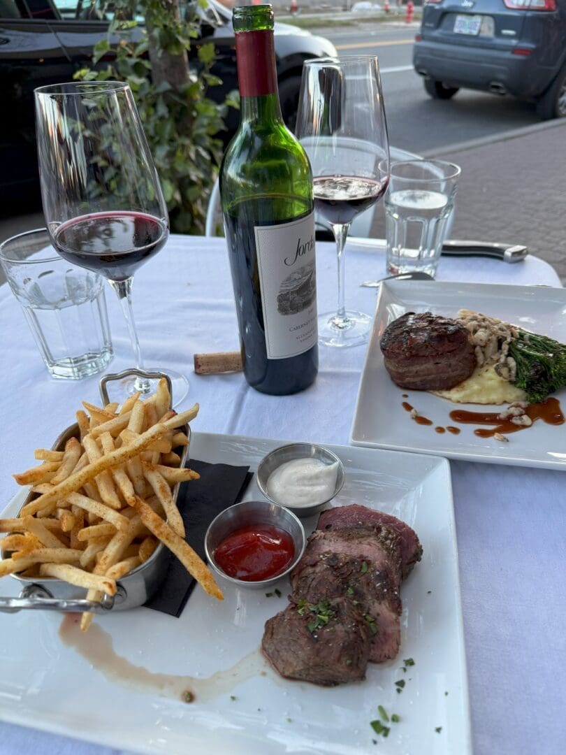 a Table Set for Two Outdoors at One of the Top Bend Restaurants Featuring a Bottle of Red Wine Fries with Ketchup Sliced Steak and a Dish with Filet Mignon Mashed Potatoes Mushrooms and Broccolini