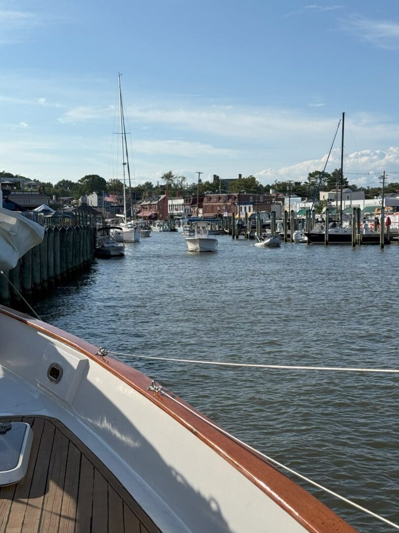View from a boat’s deck in MD showing a marina with docked boats, calm water, and waterfront buildings beneath a blue sky. Wooden piers and sailboat masts stand out—a relaxing scene among the many things to do in Frederick.