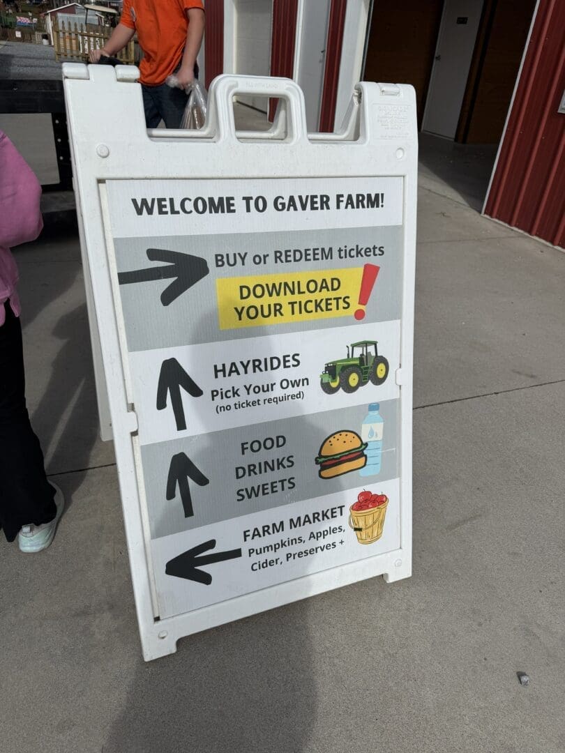 a White Sandwich Board Sign at Gaver Farm Lists Directions Buy or Redeem Tickets Hayrides with a Tractor Icon Food Drinks and Sweets with Icons and the Gaver Farm Market with Pumpkin and Preserves Symbols