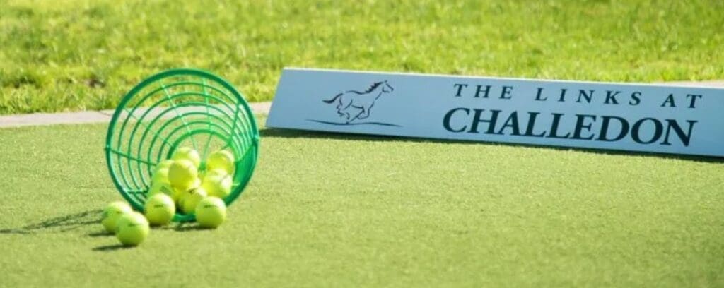 a Green Basket Tipped over on Artificial Turf Spills Tennis Balls in the Background a White Sign with a Horse Graphic Reads the Links at Challedon Highlighting This Vibrant Outdoor Sports Area Surrounded by Blurred Green Grass