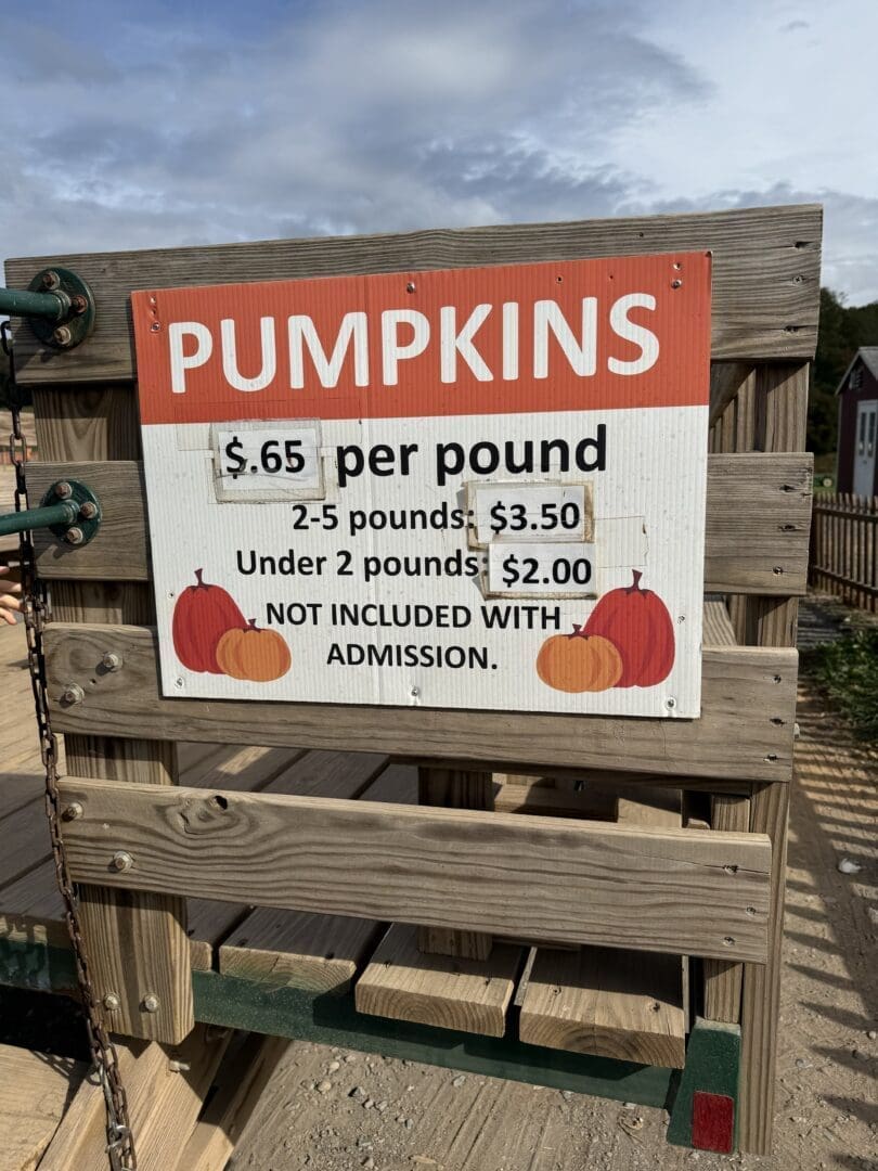 a Wooden Sign at Gaver Farm Reads Pumpkins 65¢ Per Pound 2 5 Pounds 0 Under 2 Pounds 0 Not Included with Admission the Sign with Red and Orange Pumpkins is Attached to a Wooden Fence Under a Blue Sky