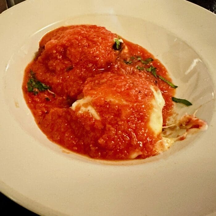 Two large ravioli topped with chunky red tomato sauce and chopped green herbs are served on a white plate at Cucina Massi Frederick MD. Melted cheese peeks through, with clean edges and slight sauce drips along one side.