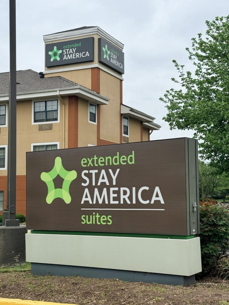Exterior View of a Stay America Sign on a Beige Building with a Green Abstract Logo and the Words Extended Stay America