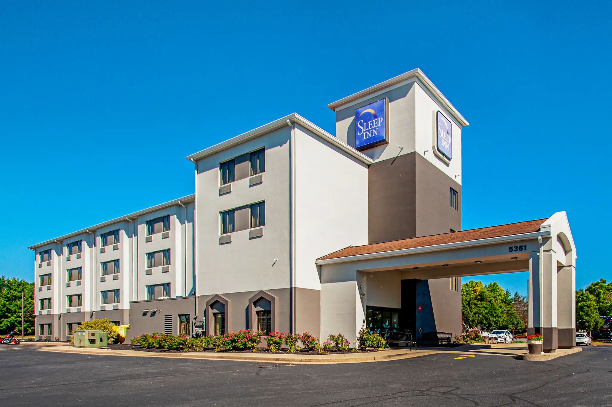 Sleep Inn hotel exterior under a clear blue sky, with a driveway and landscaped plants in front.