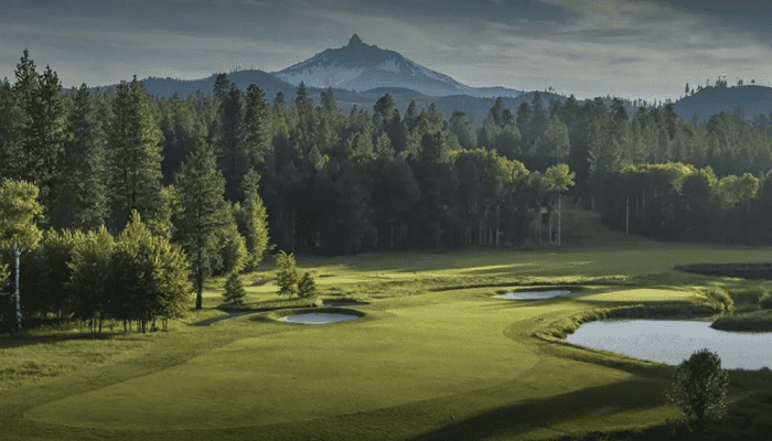 A golf course with green fairway, sand bunkers, and a water hazard, bordered by trees and distant mountains in a serene landscape.