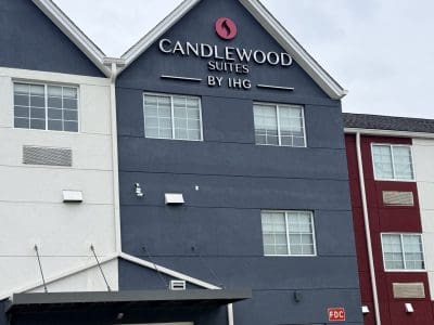 Exterior of Candlewood Suites by IHG hotel with a dark blue facade, white trim, and glass lobby doors at the entrance.