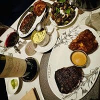 A restaurant table in Airbnb Frederick MD features plates of grilled steak, Yorkshire pudding, Brussels sprouts, sauce cups, and glasses of red wine. Artistic leaf designs decorate the plates, and the neatly arranged food looks especially appetizing.