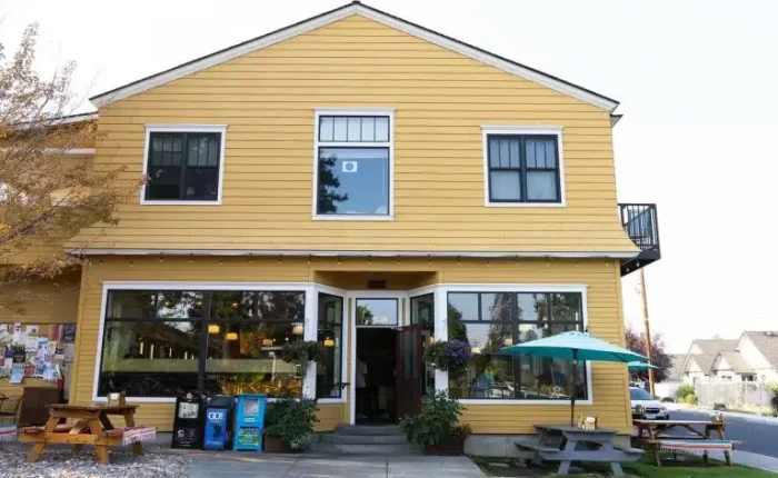 A two-story yellow building with white trim houses one of the best restaurants Bend Oregon has to offer. Large front windows, hanging flower baskets, and outdoor tables with a teal umbrella invite you in on this quiet street.