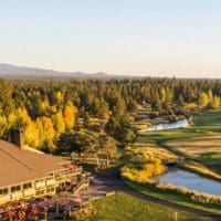 The Sunriver Lodge at Sunriver Resort with its golf course is surrounded by lush green fairways and autumn-colored trees—a picturesque choice for those seeking where to stay in Bend, Oregon, with mountain views under a golden sunset sky.
