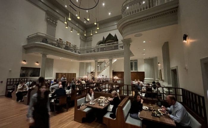 A spacious, elegant restaurant with high ceilings, chandeliers, and a balcony—perfect for guests from boutique hotels Frederick MD. Soft lighting, wooden floors, and classical details create a warm atmosphere as diners enjoy meals and attentive service.