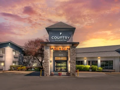 Country Inn & Suites entrance at sunset with a stone portico, illuminated sign, and potted plants in front.