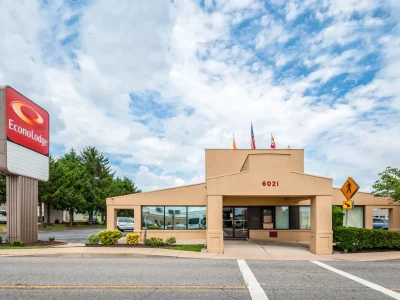 Econo Lodge hotel exterior with red sign, beige entrance, flags on the roof, and a pedestrian crossing sign against a cloudy blue sky.