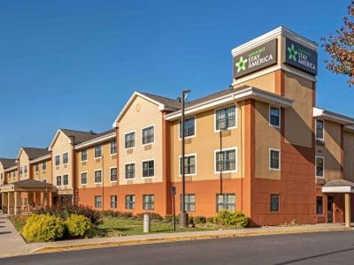 Exterior of an Extended Stay America hotel with tan and orange walls, multiple windows, and a clear blue sky above.
