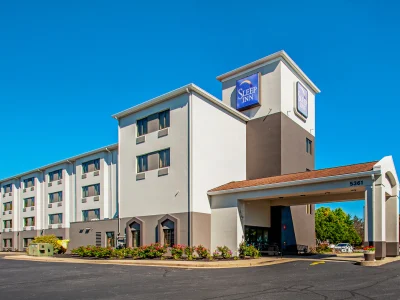 Sleep Inn hotel exterior under a clear blue sky, with a driveway and landscaped plants in front.